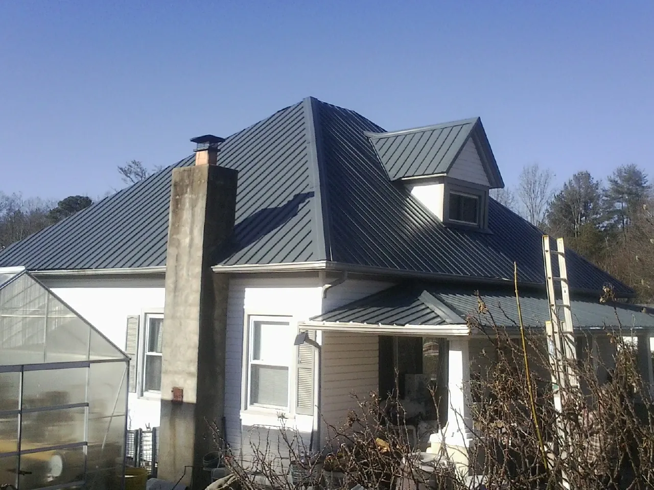 Dark blue standing seam metal roof on a white farmhouse with dormer — Slate & Tile Roof Repair by Roofing Brothers in Belfry