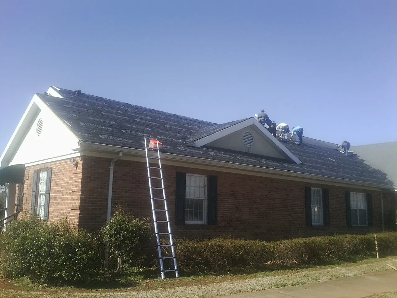 Crew tearing shingles off a brick ranch roof with a ladder set — Emergency Roof Repair work by our crew in Belfry