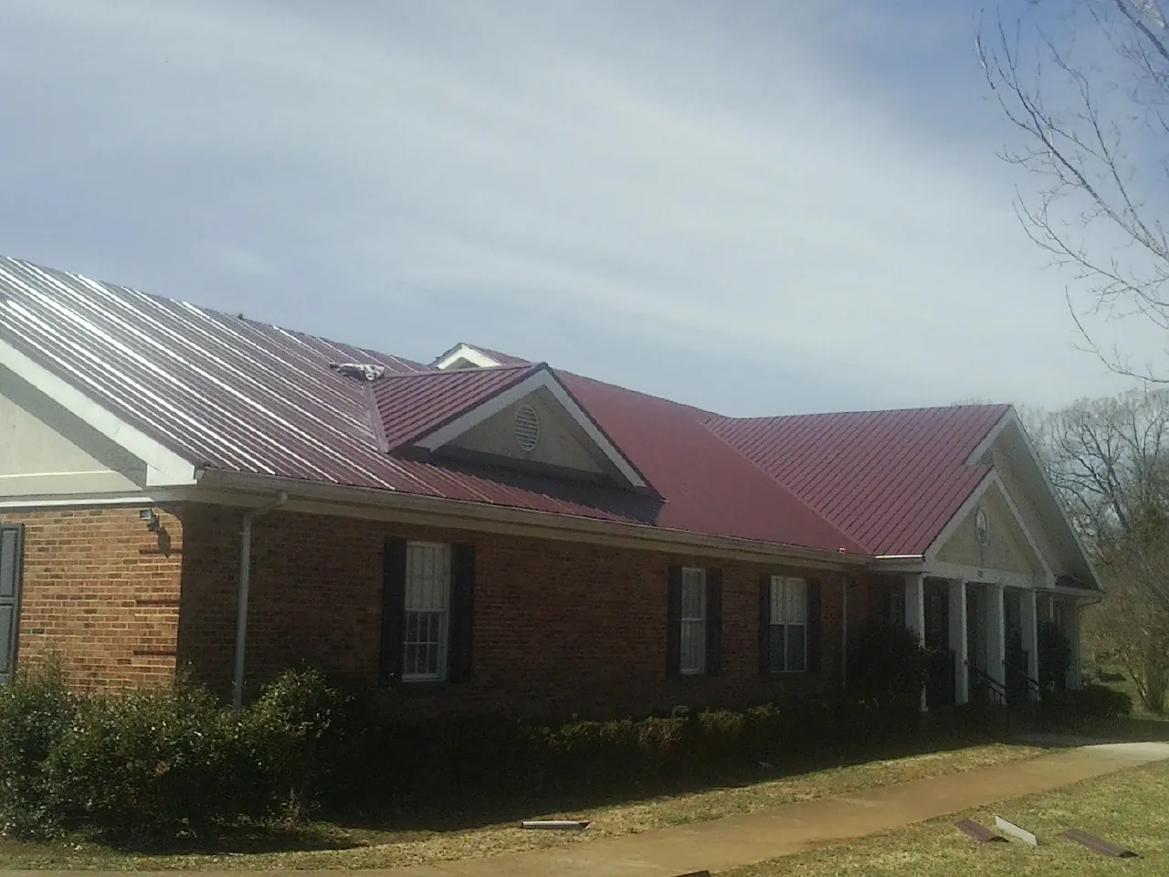 Red metal roof with gabled entries on a long brick building, from a Hail Damage Roof Repair job in Belfry
