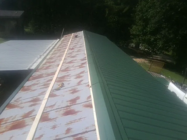 Old rusted panels beside newly installed green metal roofing — Wind Damage Roof Repair by Roofing Brothers in Belfry