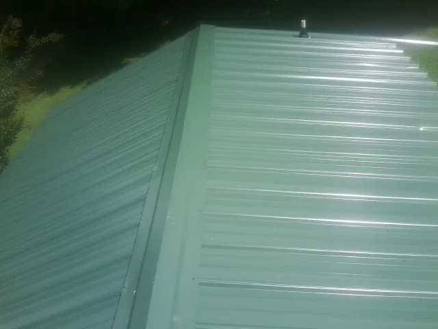 New green metal panels meeting at the ridge of a roof — Flat Roof Repair work by our crew in Belfry