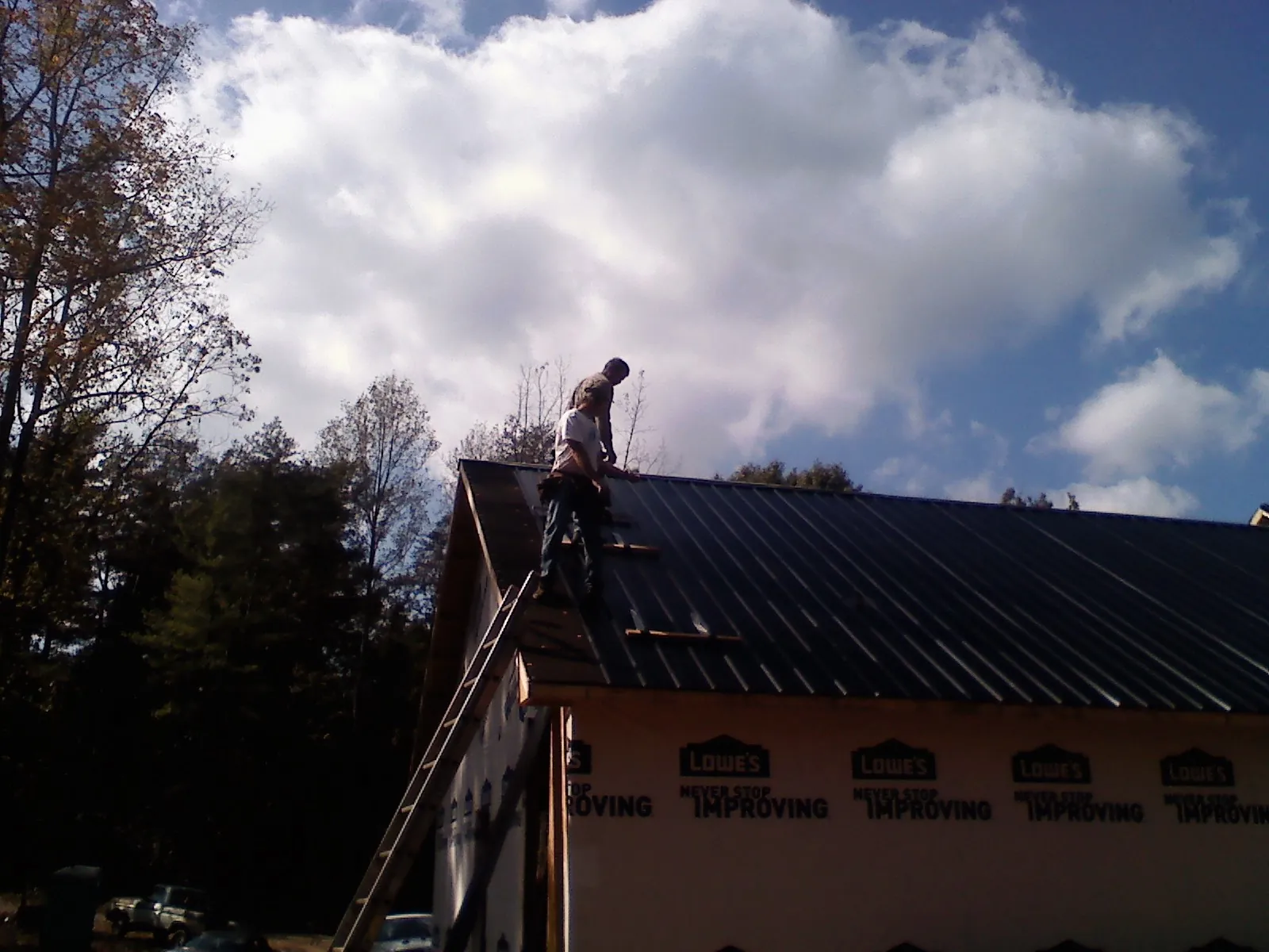 Roofer fastening dark metal panels high against a cloudy sky, from a Roof Inspection job in Belfry