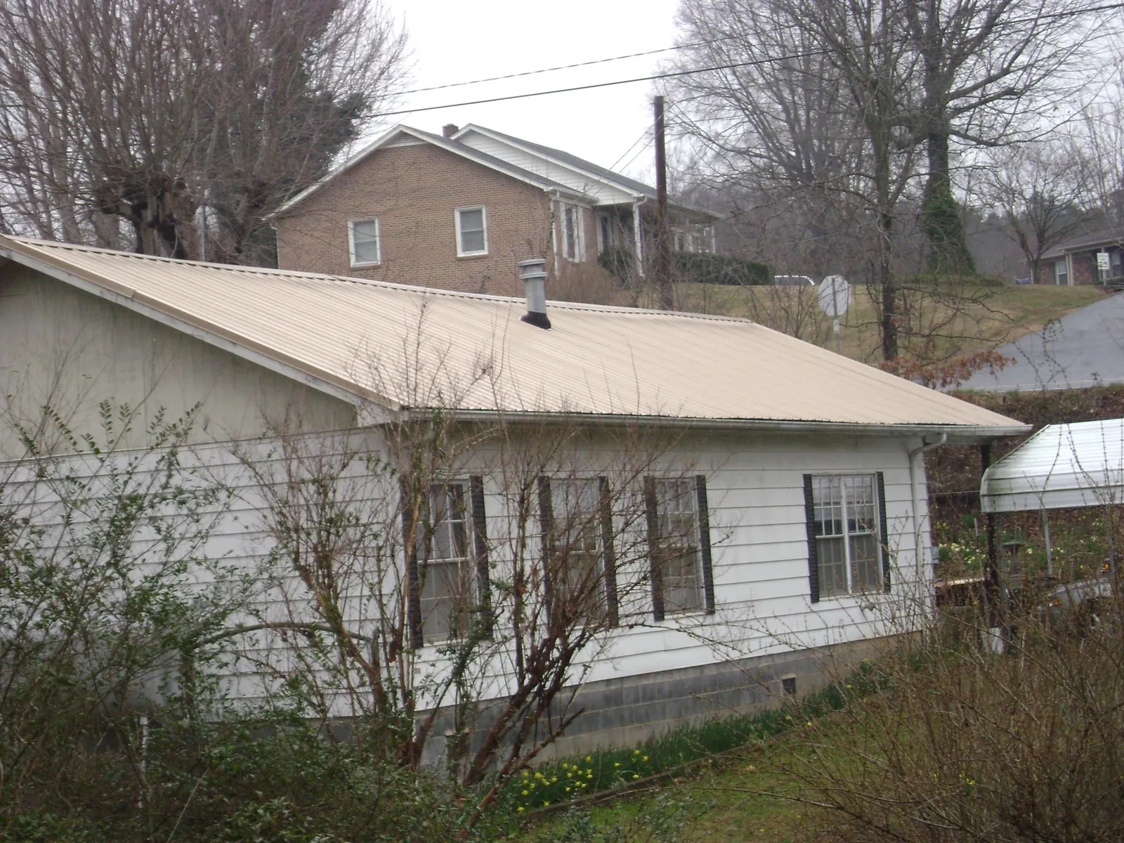 Tan metal roof on a white sided house set into a hillside — Commercial Roofing by Roofing Brothers in Belfry