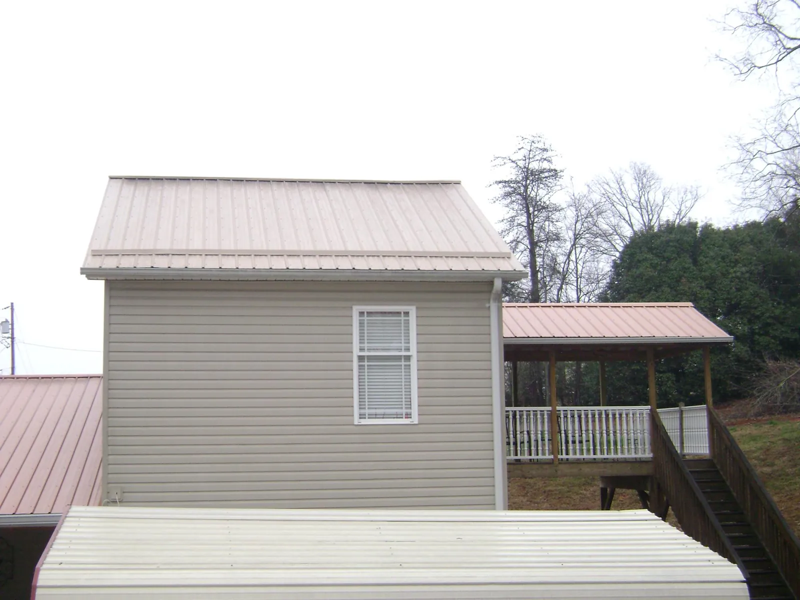 Tan metal roofs on a two story addition and attached porch, from a Roof Replacement job in Belfry