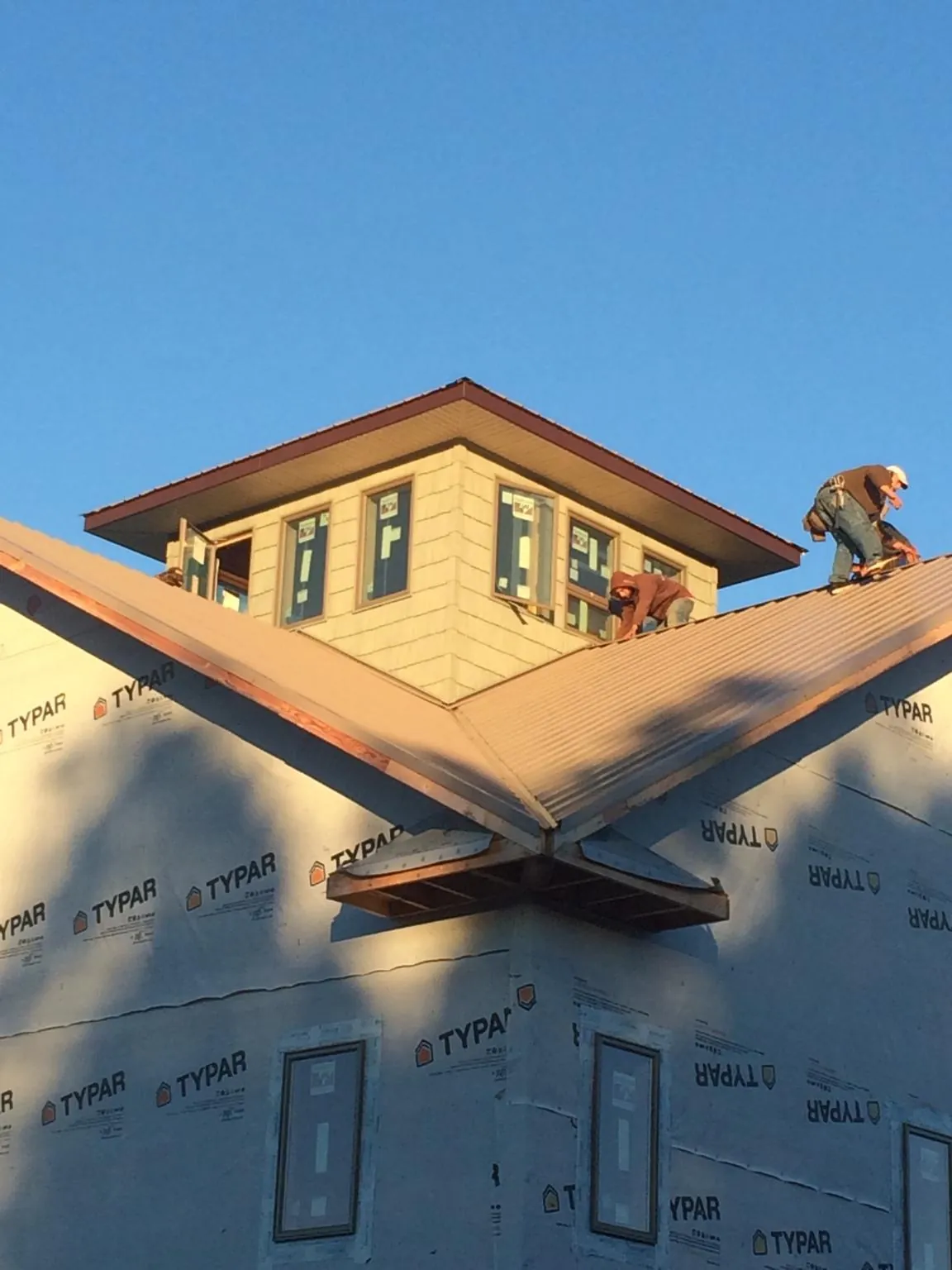 Roofers working around a rooftop cupola on a new metal roof at sunset — Roof Waterproofing in Belfry by Roofing Brothers